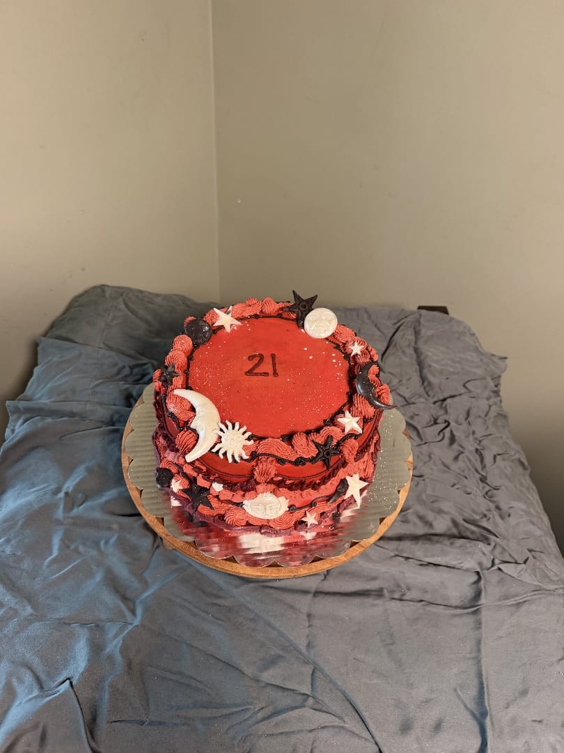 Round red cake decorated with frosted moons and stars and marked 21