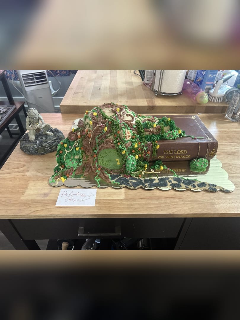 Storybook-themed cake shaped like a green hillside with a round door, sitting on a book