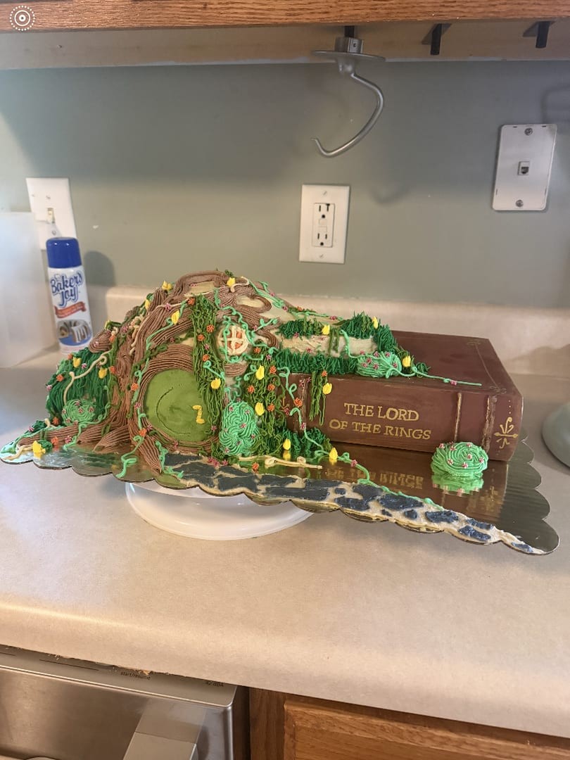 Green hillside cake with a round door and twinkle lights on a book-shaped base