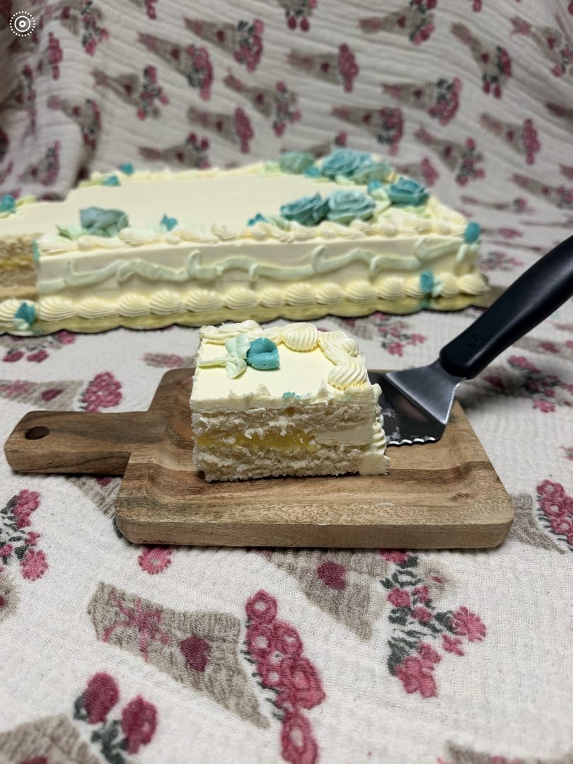 Sheet cake with blue frosting flowers and one slice cut out, served on a wooden board