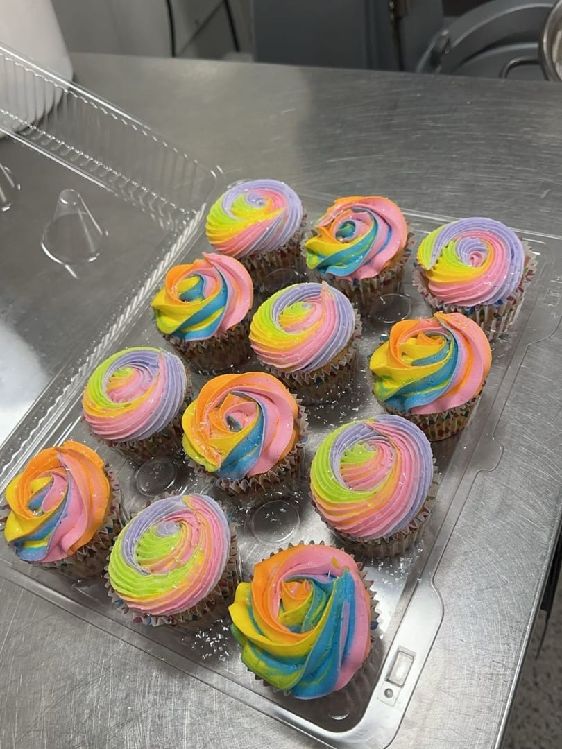 A dozen rainbow-swirl cupcakes in a clear container