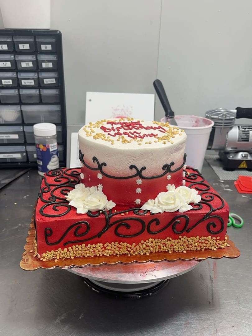Two-tier red and white cake with black scrollwork piping and white roses