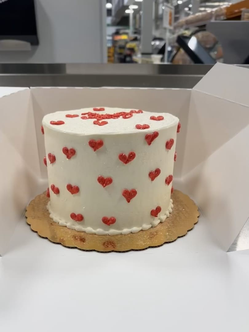 White cake covered in tiny red hearts, in a cake box