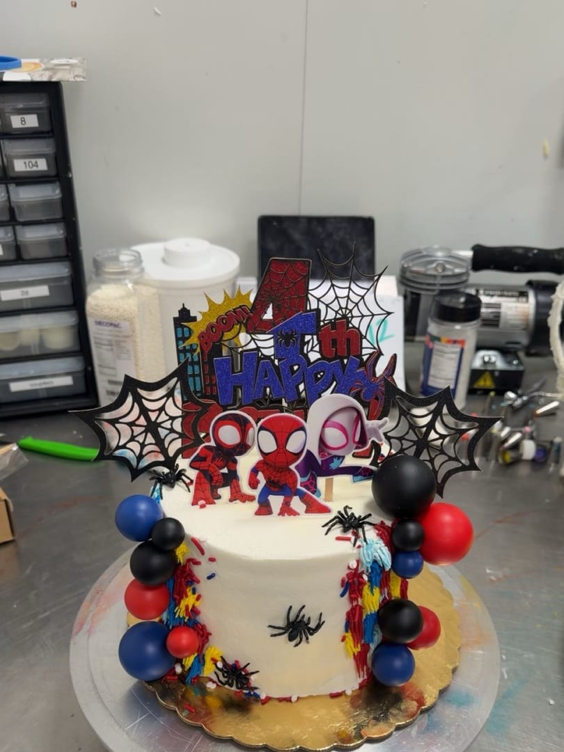 Spider-themed birthday cake with black, red, and blue balloons and web decorations