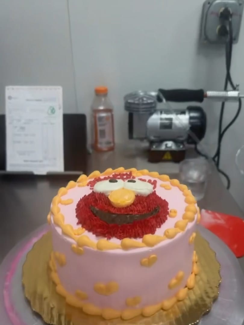 Small pink cake topped with a red character face and yellow piped borders