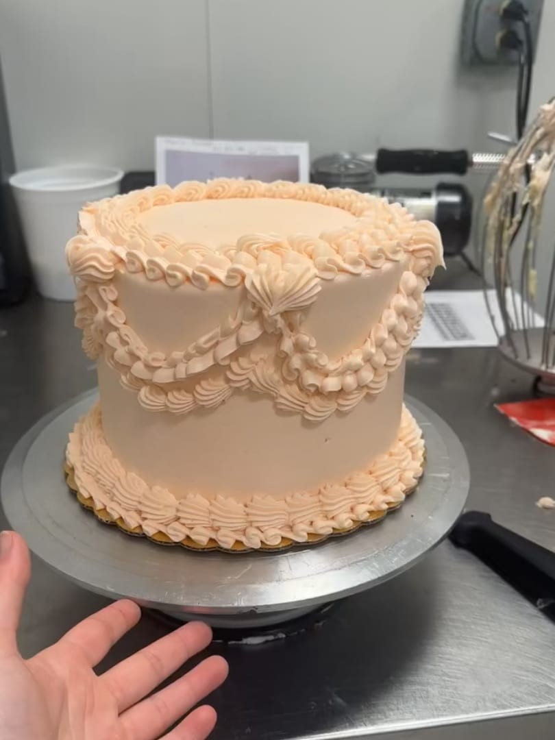 Round cake with peach ruffled frosting and swag piping