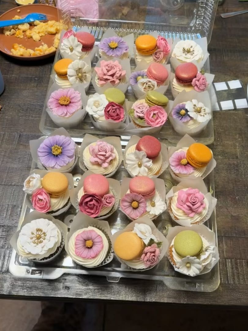 Two trays of cupcakes topped with pastel flowers and macarons