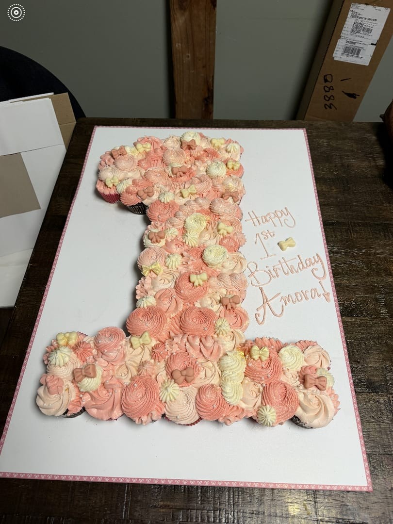 Number-one cupcake cake made of pink and cream frosted cupcakes on a white board