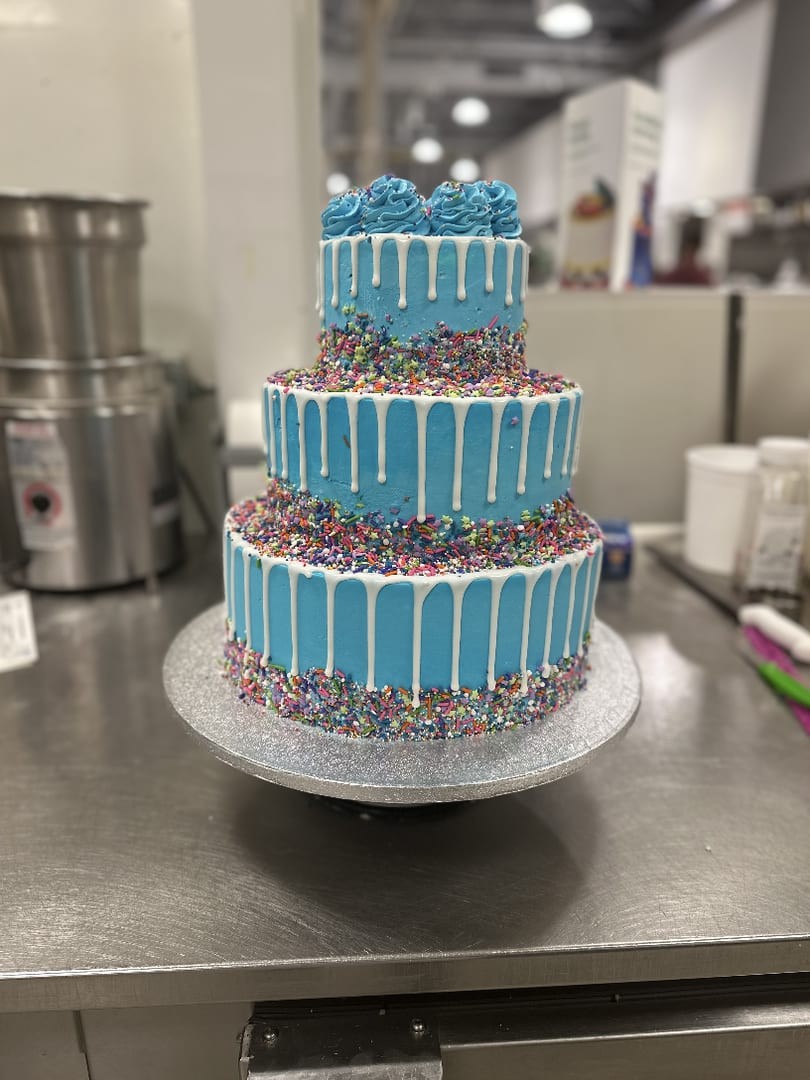 Three-tier cake with blue drip stripes and rainbow sprinkles